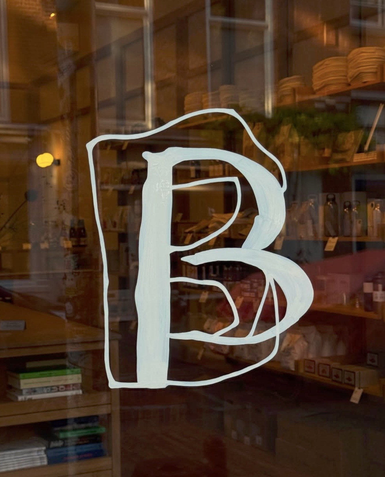A hand-painted B decal on the front window, market shelves of books, jars and bottles visible through the glass behind it